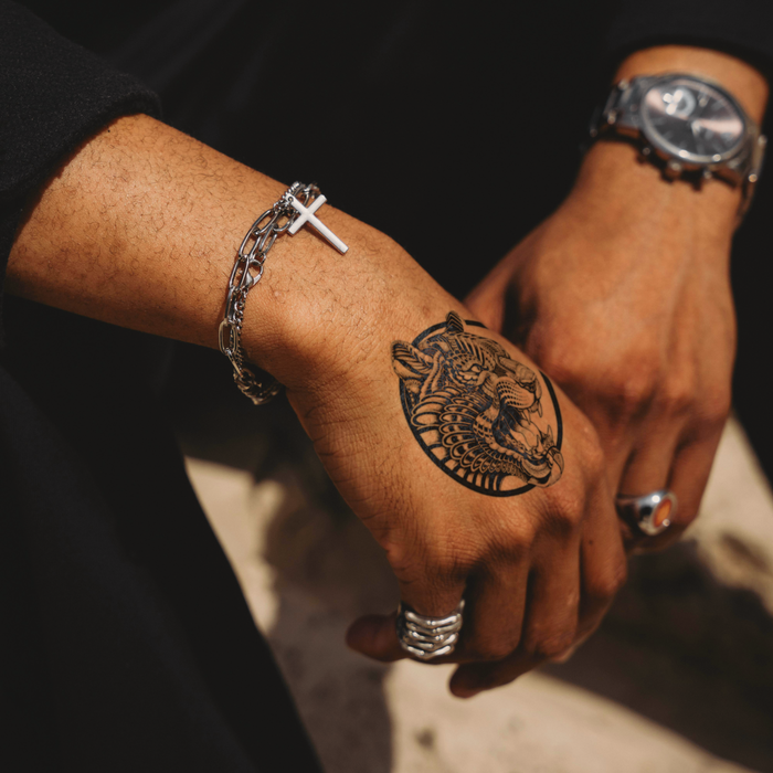 Hand with tiger tattoo wearing silver bracelet and watch, close-up