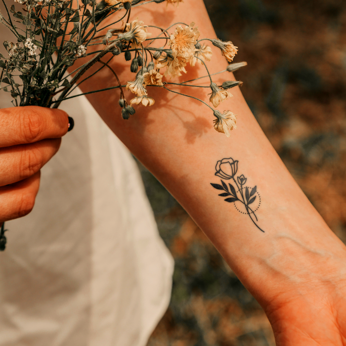 Person holding a small bouquet of flowers with a floral tattoo on their arm.
