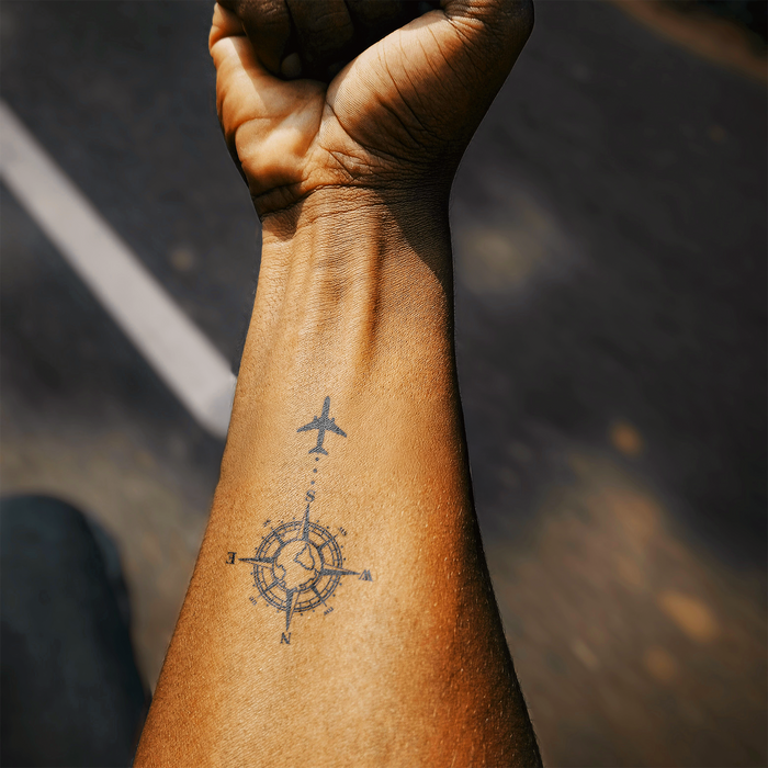 Hand with a tattoo of a compass and airplane on a blurred background
