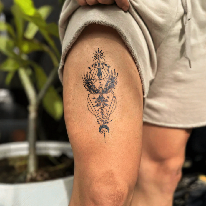 Tattoo of an eagle and geometric design on a person's leg with a blurred natural background
