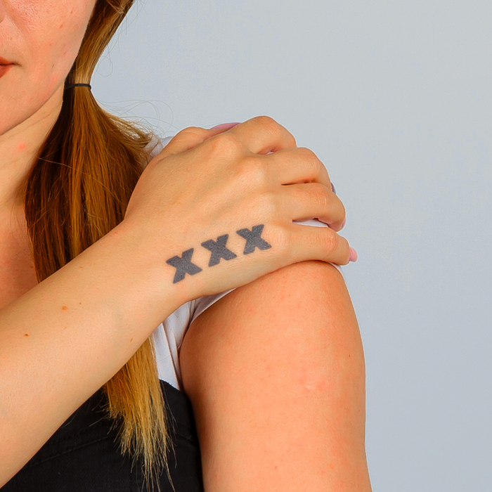 Person with a tattoo of 'XXX' on their wrist against a plain background