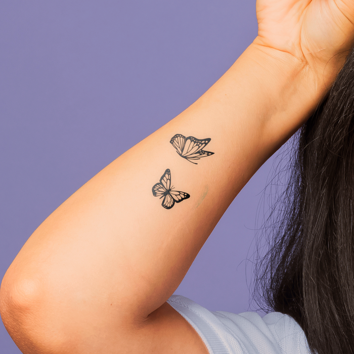 Two butterfly tattoos on a person's arm against a purple background