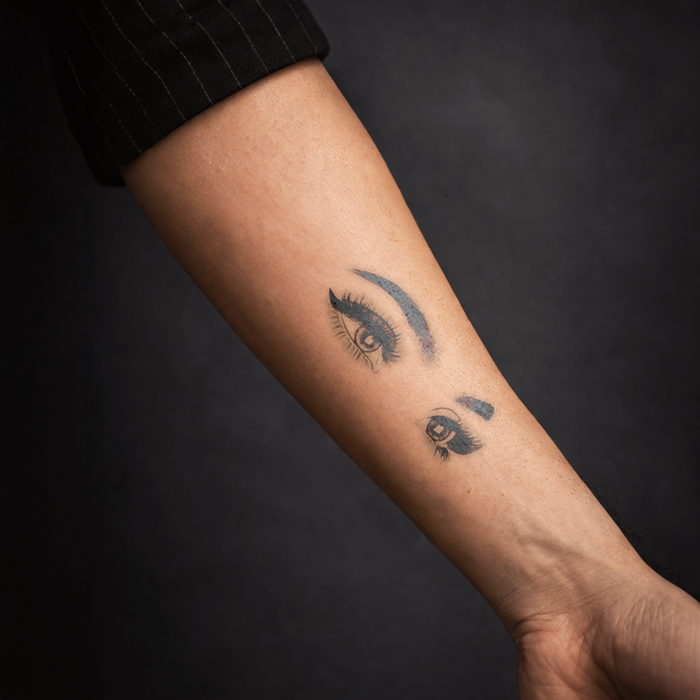 Tattoo of eyes on a person's arm against a dark background