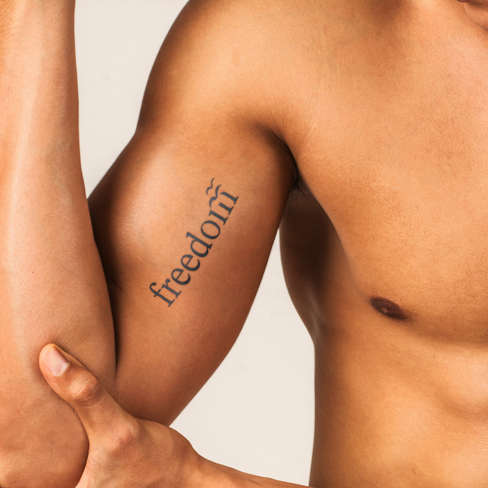 Person with 'freedom' tattoo on arm against a neutral background